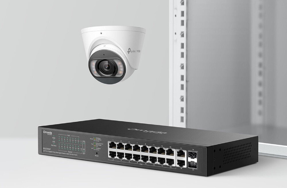 Switch TP-LINK Omada ES220GP Przełącznik sieciowy leżący na jasnym tle, nad którym unosi się biała, kopułowa kamera monitoringu z widocznym obiektywem i diodami, opis