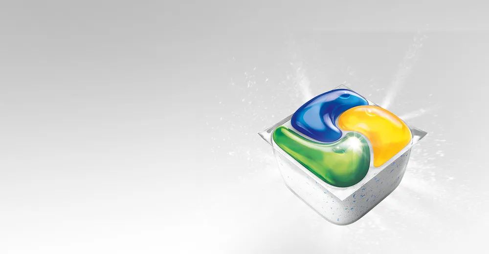 Czterokolorowa kapsułka do zmywarki Fairy Platinum na jasnym tle z rozpryskiem detergentu