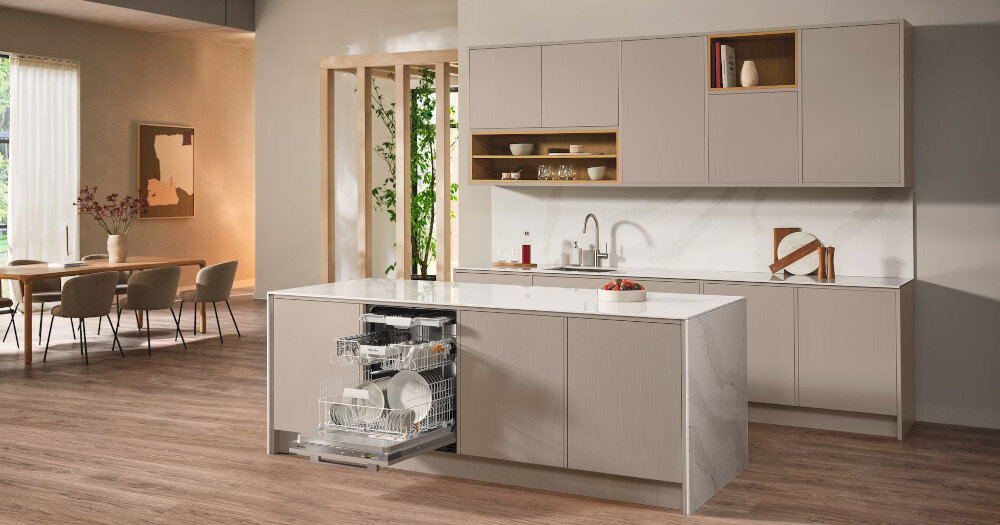 ZMYWARKA MIELE G5651 ACTIVE Zdjęcie przedstawia przestronną kuchnię z wyspą, w której zamontowana jest otwarta zmywarka wypełniona naczyniami. Jasna kolorystyka, eleganckie fronty meblowe i minimalistyczny układ nadają wnętrzu stylowy i funkcjonalny charakter