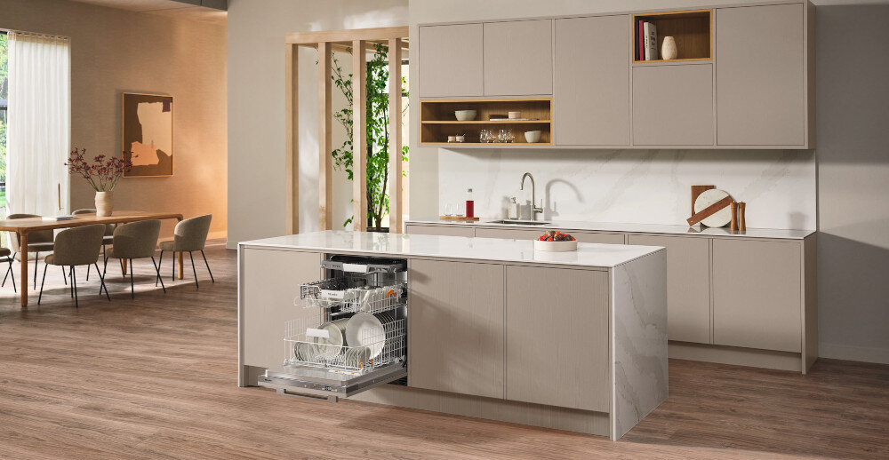 ZMYWARKA MIELE G 5851 SCVi Active Plus Zdjęcie przedstawia przestronną kuchnię z wyspą, w której zamontowana jest otwarta zmywarka wypełniona naczyniami. Jasna kolorystyka, eleganckie fronty meblowe i minimalistyczny układ nadają wnętrzu stylowy i funkcjonalny charakter