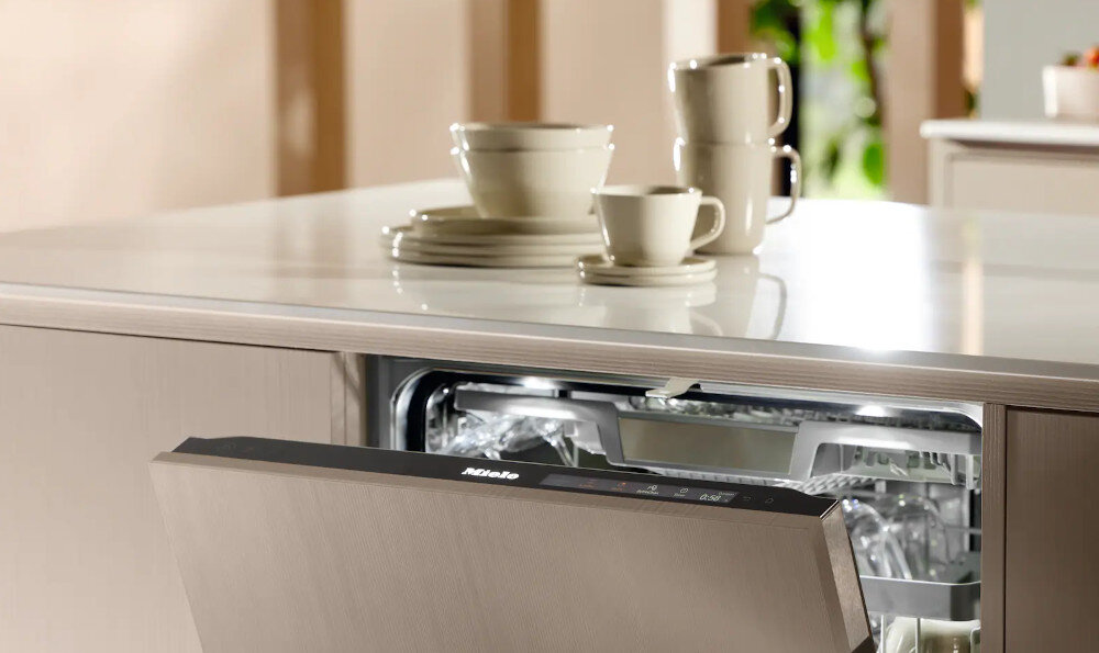 ZMYWARKA MIELE G 5851 SCVi Active Plus Zdjęcie ukazuje otwartą zmywarkę w zabudowie, z której delikatnie wydobywa się światło oświetlające jej wnętrze. Na blacie nad urządzeniem ustawiono zestaw czystych naczyń, co podkreśla skuteczność mycia i funkcjonalność kuchni opcja Quick 58 minut Quick PowerWash krótszy czas szybkie suszenie