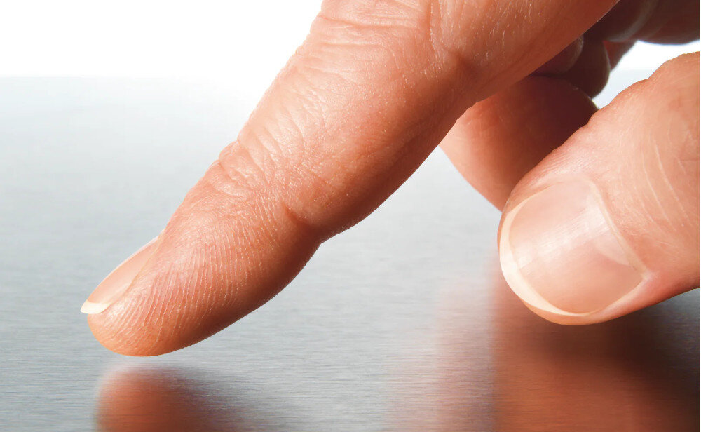 ZMYWARKA MIELE G 7040 SCi AutoDos CS Zdjęcie przedstawia zbliżenie palców dotykających powierzchni ze stali nierdzewnej o delikatnej, szczotkowanej strukturze. Ujęcie podkreśla odporność materiału na odciski palców oraz jego eleganckie, matowe wykończenie powłoka CleanSteel mniej odcisków palców łatwe czyszczenie stal szlachetna