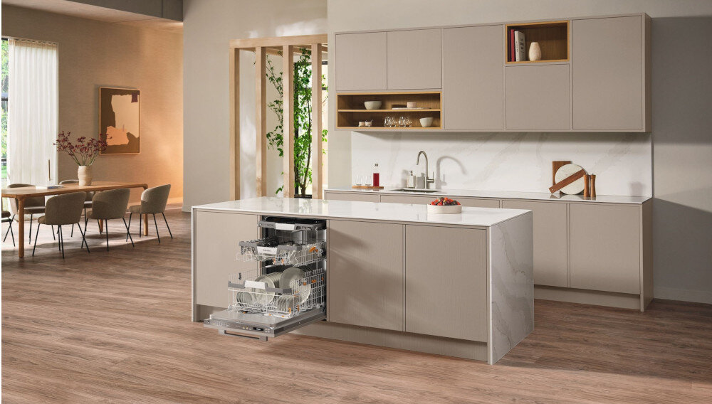 ZMYWARKA MIELE G7085 SCVI XXL Zdjęcie przedstawia przestronną kuchnię z wyspą, w której zamontowana jest otwarta zmywarka wypełniona naczyniami. Jasna kolorystyka, eleganckie fronty meblowe i minimalistyczny układ nadają wnętrzu stylowy i funkcjonalny charakter