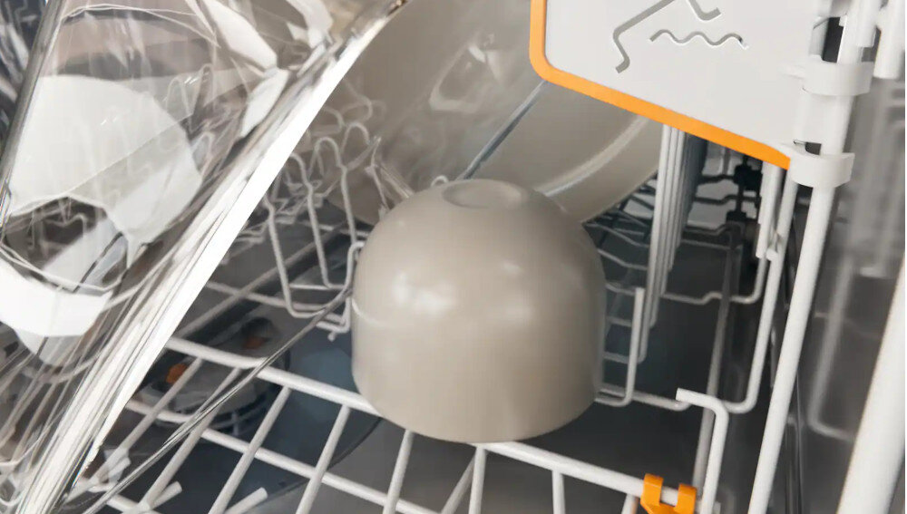 ZMYWARKA MIELE G7085 SCVI XXL Zdjęcie przedstawia dno zmywarki, w którym umieszczono szarą miseczkę odwróconą do góry dnem na dolnym koszu urządzenia. Widoczne oznaczenia i elementy regulacyjne w kolorze pomarańczowym podkreślają możliwość stabilnego rozmieszczenia naczyń oraz bezpieczeństwo podczas mycia XL-Assist duże naczynia elastyczne układanie kosz dolny optymalne rozmieszczenie łatwe składanie