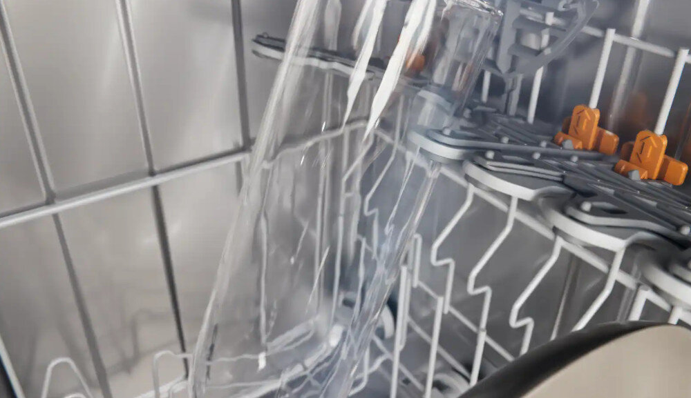 ZMYWARKA MIELE G7085 SCVI XXL Zdjęcie przedstawia wnętrze zmywarki z umieszczoną w koszu szklaną karafką, która jest stabilnie podparta dzięki specjalnym uchwytom na szkło. Ujęcie podkreśla delikatną pielęgnację naczyń oraz bezpieczne mycie nawet wysokich, smukłych elementów BottleClean czyszczenie butelek wielokrotnego użytku FlexCare Glass Bottle dokładne mycie naczyń z pustką szybki program