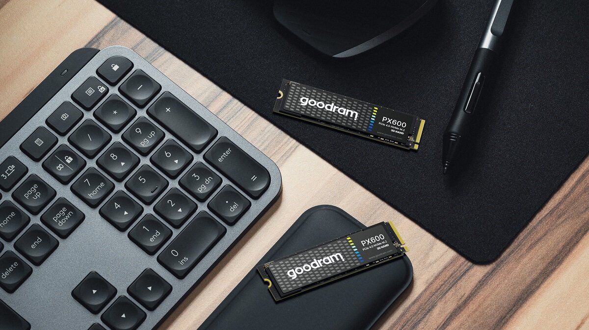 Na drewnianym biurku leży klawiatura, mysz, pióro oraz dwa dyski SSD z napisem \'goodram PX600\'.