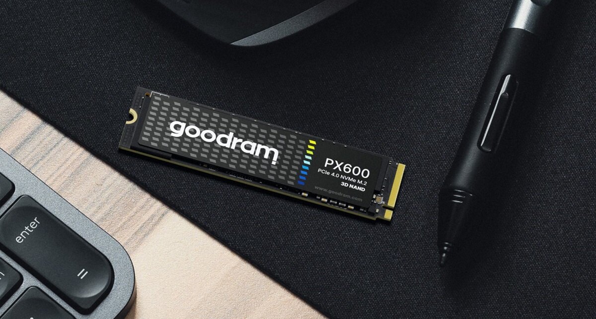 Na obrazie znajduje się dysk SSD GOODRAM PX600 z oznaczeniami \'PCIe 4.0 NVMe M.2\' i \'3D NAND\', leżący na ciemnej powierzchni obok klawiatury i pióra cyfrowego.