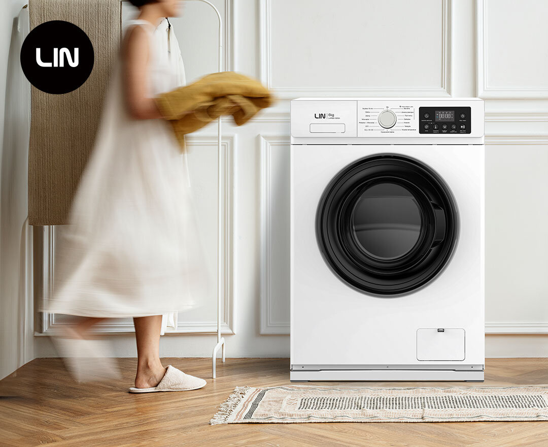PODSTAWA POD PRALKĘ I SUSZARKĘ LIN LI10W To zdjęcie przedstawia kobietę idącą w stronę białej pralki automatycznej marki LIN. Pralka stoi w stylowym, domowym wnętrzu na podłodze z drewnianych paneli.