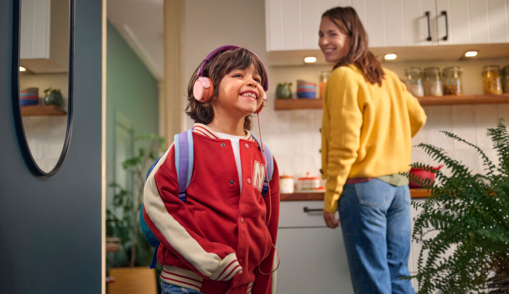 Słuchawki nauszne PHILIPS TAK2000CT mikrofon i redukcja szumów dla rozmów, dziecko z założonymi słuchawkami nausznymi, rodzic stojący przy szafkach kuchennych