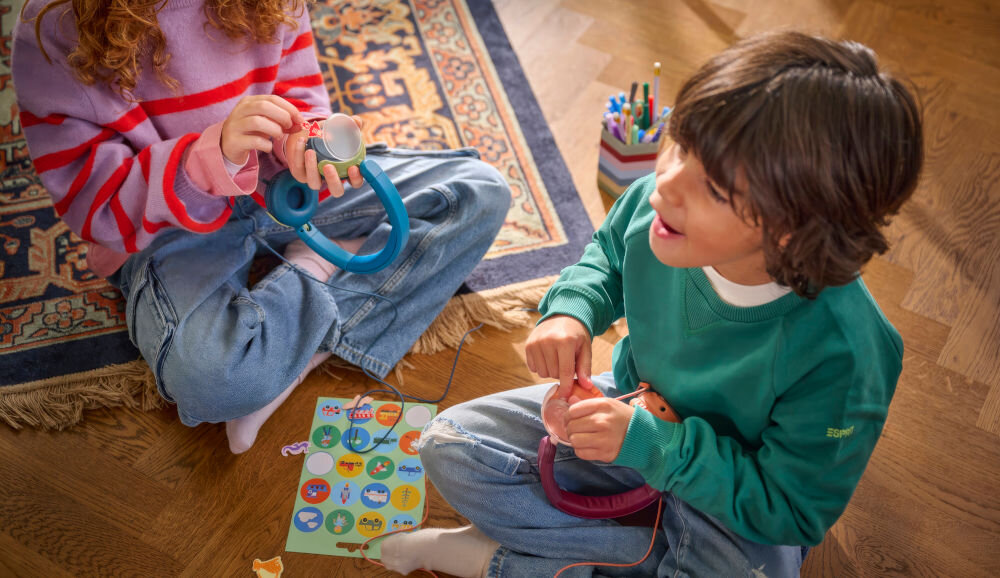 Słuchawki nauszne PHILIPS TAK2000CT ciepły naturalny dźwięk z przetwornikami 32 mm, dzieci siedzące po turecku na podłodze mające słuchawki w rękach