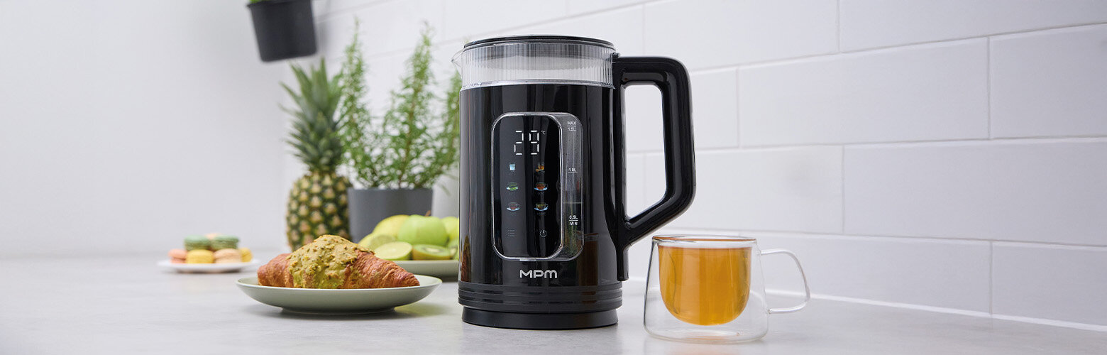 Czajnik na kuchennym blacie. Obok szklanka z napojem i rogalik na talerzu.