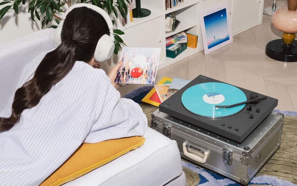 Gramofon SONY PS-LX3BT Bluetooth aptX Adaptive bezprzewodowe audio, gramofon stojący na walizce , osoba z załozonymi słuchawkami leżąca na kanapie