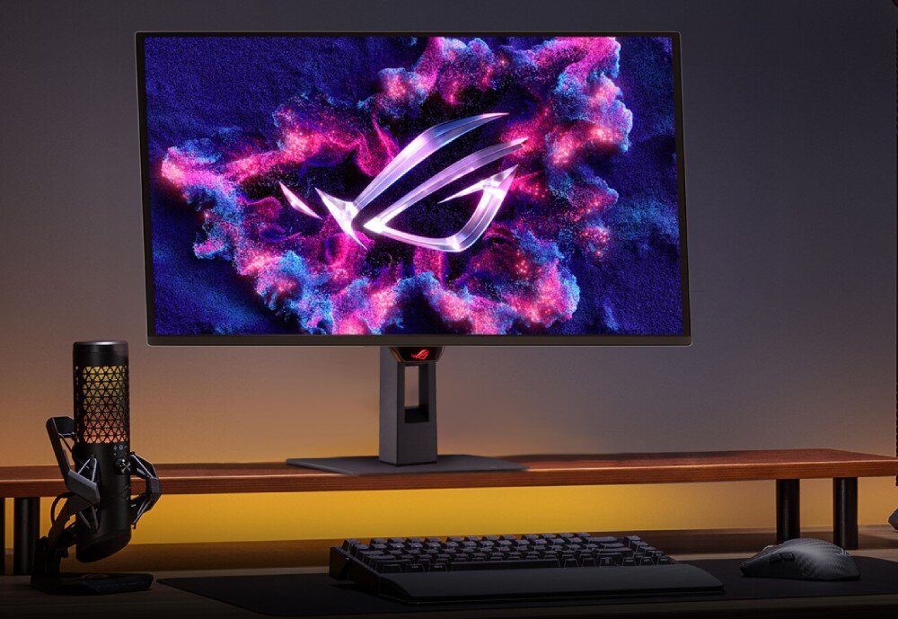 Monitor ASUS ROG Strix XG27AQDMES Monitor z kolorową grafiką na ekranie stoi na drewnianej podstawce na biurku, obok znajduje się mikrofon, klawiatura i mysz