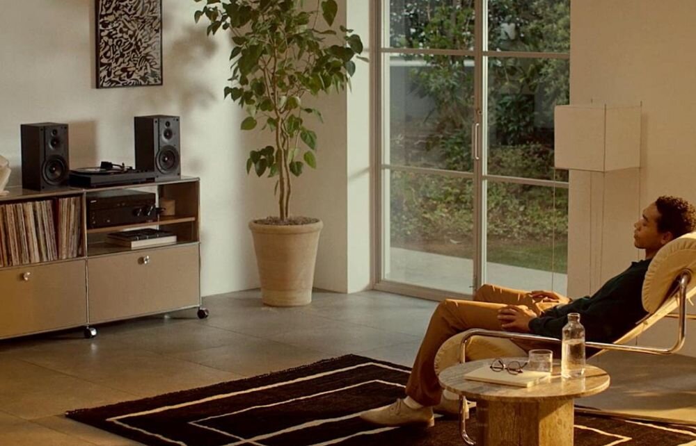 Gramofon SONY PS-LX5BT pozłacane zaciski wyjściowe czysty transfer sygnałum osoba siedząca w fotelu, gramofon stojący na komodzie w pomieszczeniu