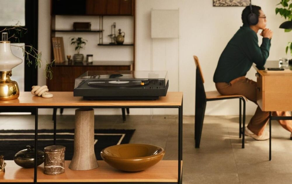 Gramofon SONY PS-LX5BT Bluetooth aptX Adaptive bezprzewodowe audio, osoba siedząca przy stole w słuchawkach nausznych, gramofon stojący na na szefce w pomieszczeniu