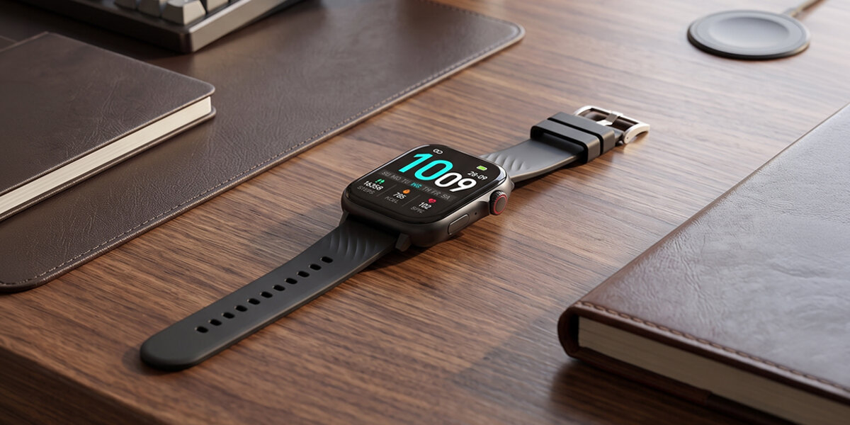 Na biurku leży smartwatch Denver. Obok znajduje się skórzany notes oraz fragment klawiatury.