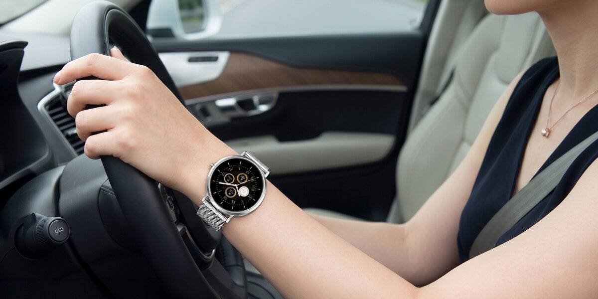 Kobieta trzyma dłoń na kierownicy auta. Na jej nadgarstku znajduje się srebrny smartwatch Denver z czarną tarczą.