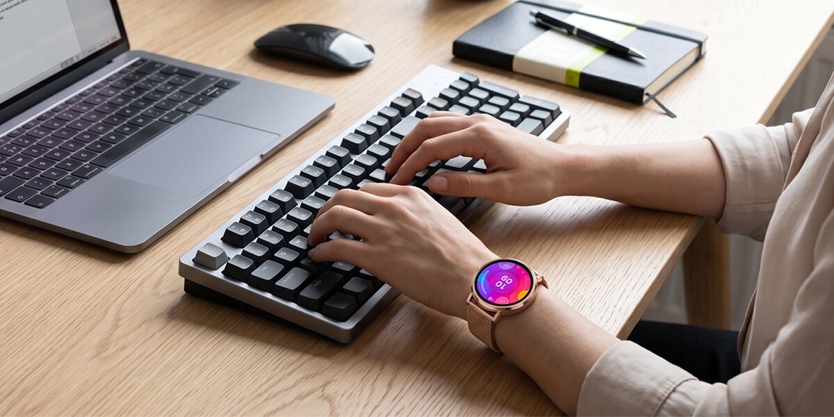 Dłonie piszą na klawiaturze komputera. Na nadgarstku znajduje się smartwatch Denver z kolorową tarczą.