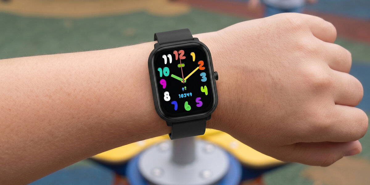 Zielony smartwatch Denver dla dzieci na nadgarstku, wyświetla kolorową tarczę z zegarem i krokomierzem na tle placu zabaw.