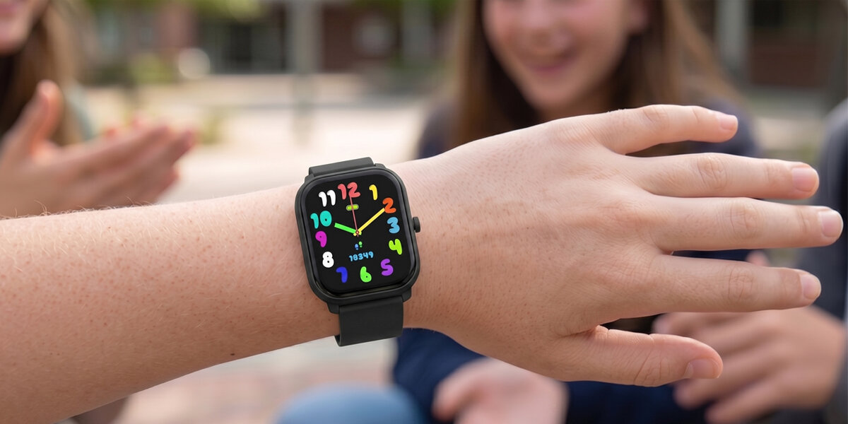 Dziecko prezentuje zielony smartwatch Denver rówieśnikom - kolorowa tarcza z zegarem i liczbą kroków widoczna na nadgarstku.