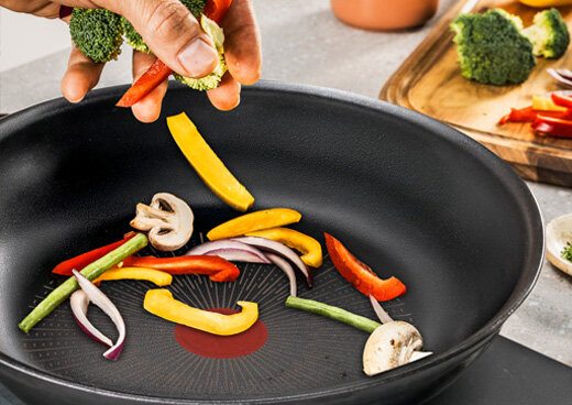 Osoba wrzuca różne warzywa na patelnię TEFAL Excellence+ G3301902.
