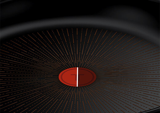 Wnętrze patelni z widocznym czerwonym wskaźnikiem temperatury na środku. Powierzchnia patelni ma wzór promieniście rozchodzących się linii.