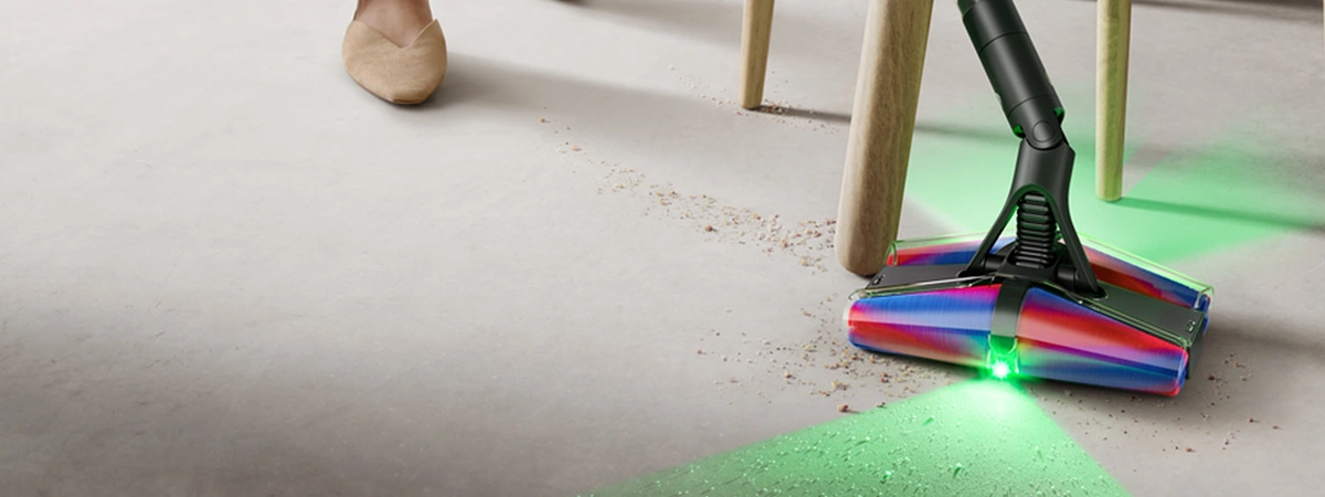 Elektroszczotka manewruje między stołem i krzesłami podczas sprzątania podłogi z dużych okruchów i kurzu