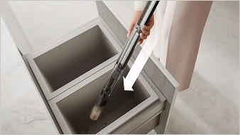 Osoba trzyma w dłoni pojemnik nad koszem i opróżnia go z nieczystości oraz brudu po zakończonym sprzątaniu