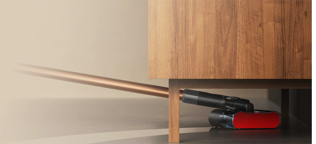 Elektroszczotka jest głęboko wsunięta pod mebel na nóżkach i zmywa trudno dostępną powierzchnię podłogi