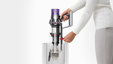 Osoba opróżnia pojemnik odkurzacza do białego kosza. Odkurzacz ma fioletowy element na górze i przezroczysty pojemnik na kurz.