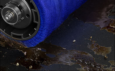 Na obrazie widoczna jest niebieska szczotka odkurzacza, która przesuwa się po powierzchni pokrytej ciemną cieczą i drobnymi zanieczyszczeniami.