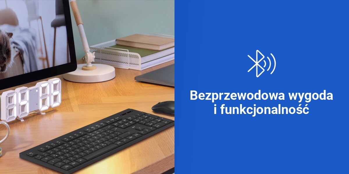 Na biurku znajduje się czarna klawiatura, obok której stoi monitor, lampka i zegar cyfrowy. Po prawej stronie widoczny jest niebieski panel z ikoną Bluetooth i napisem \'Bezprzewodowa wygoda i funkcjonalność\'.
