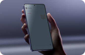 Osoba trzyma smartfon z widocznym ekranem, na którym jest otwarta aplikacja do wiadomości z tekstem \'Maddie\' i emotikoną kota. Tło jest rozmyte i ma szary odcień.