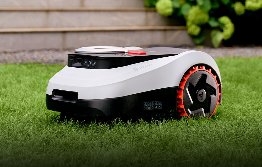 Robot koszący SEGWAY NAVIMOW i220E ogród trawnik robot stoi na trawie w tle schody wydajny akumulator o pojemności 10 Ah czas pracy 120 minut czas pełnego ładowania wynosi około 120 minut