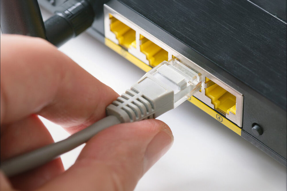 Osoba podłącza kabel RJ-45 do portu w urządzeniu sieciowym z kilkoma żółtymi gniazdami.