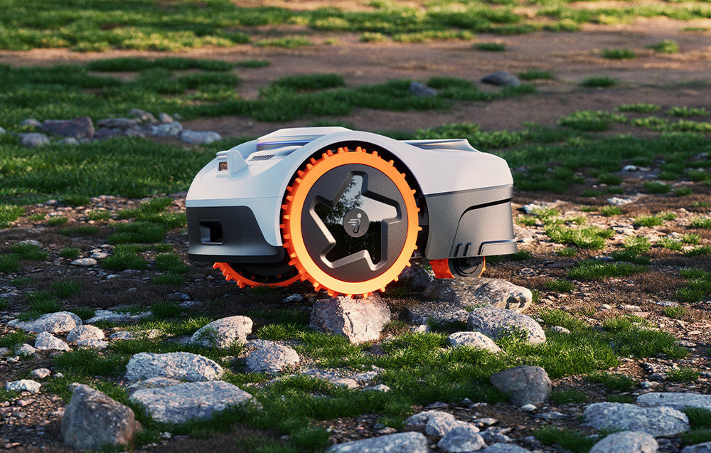 Robot koszący SEGWAY NAVIMOW i206E ogród robot ustawiony na podłożu wyłożonym dużymi kamieniami i trawą generuje hałas na poziomie zaledwie 59 dB(A) wodoodporność na poziomie IP66 przed deszczem i pyłem wbudowane czujniki wykrywają ekstremalne warunki pogodowe