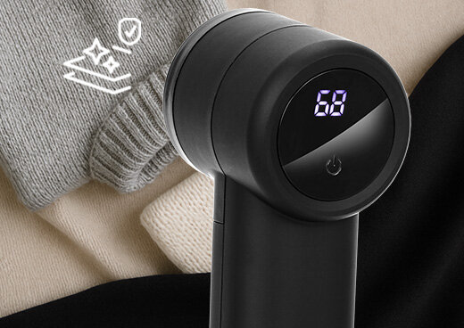 Golarka do ubrań MMU-05 z liczbą 68 na wyświetlaczu. Urządzenie przyłożone do swetra. Ikona gwiazdek i tarczy.