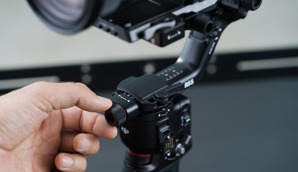 Gimbal DJI RS 5 Ręka dotykająca cylindrycznego pokrętła gimbalów podczas pracy, z aparatem zamontowanym w stabilizatorze