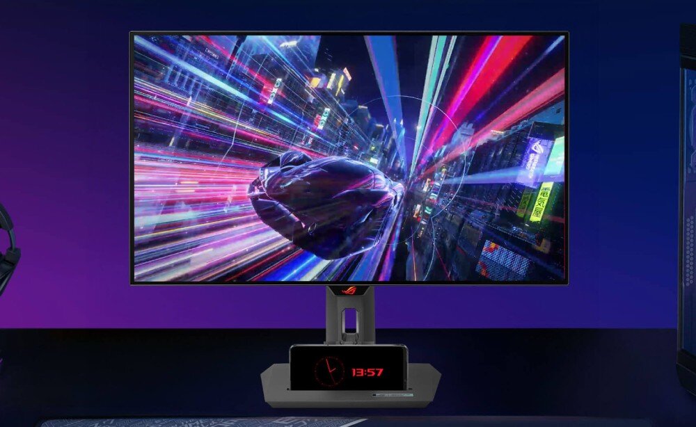 Monitor ASUS ROG Strix XG27AQDMG Monitor prezentujący dynamiczną grafikę z pędzącym pojazdem w mieście pełnym neonów. Pod ekranem znajduje się stojak z ustawionym poziomo smartfonem pokazującym godzinę, matryca, przekątna, rozdzielczość, odświeżanie, czas reakcji