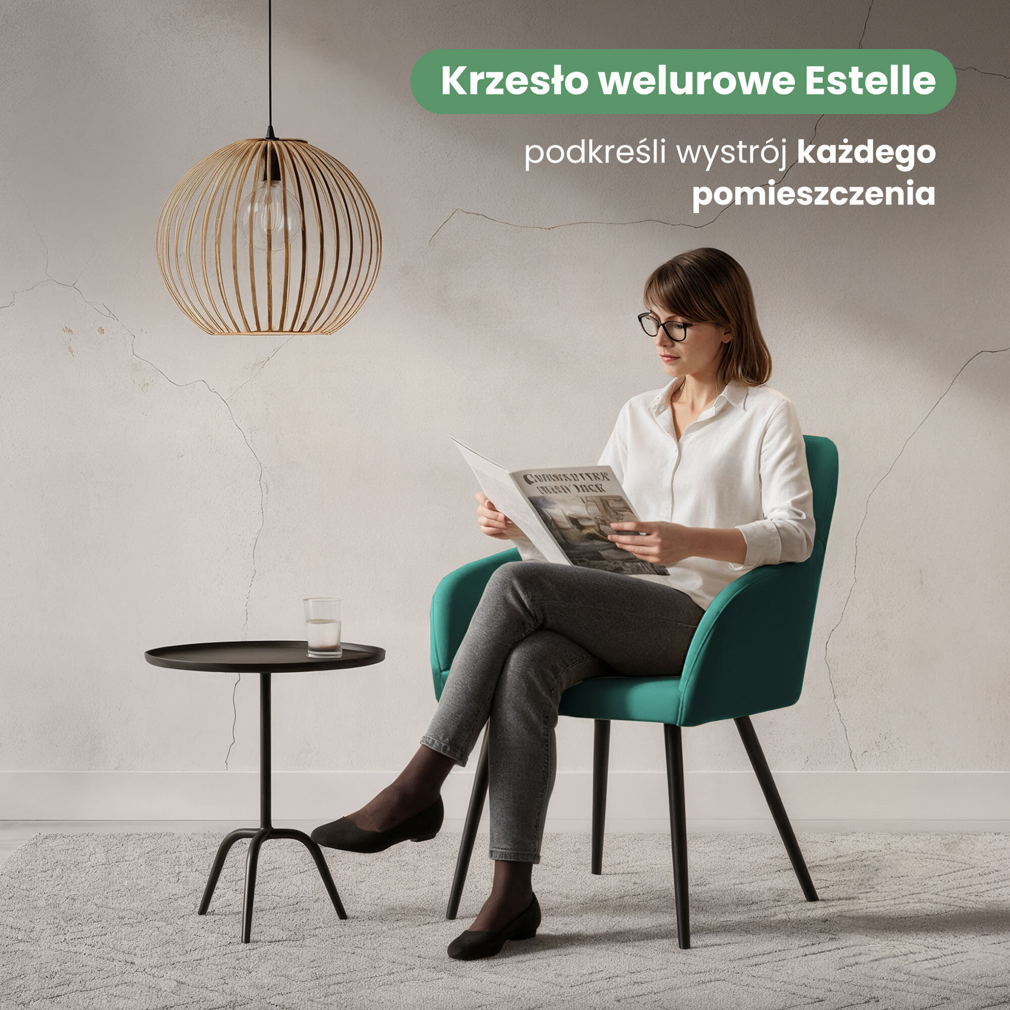 Osoba siedzi na welurowym krześle w kolorze butelkowej zieleni z czarnymi nogami, trzymając gazetę. Obok znajduje się mały stolik z szklanką, a nad nim wisi lampa; tekst na obrazie: \'Krzesło welurowe Estelle podkreśli wystrój każdego pomieszczenia\'.