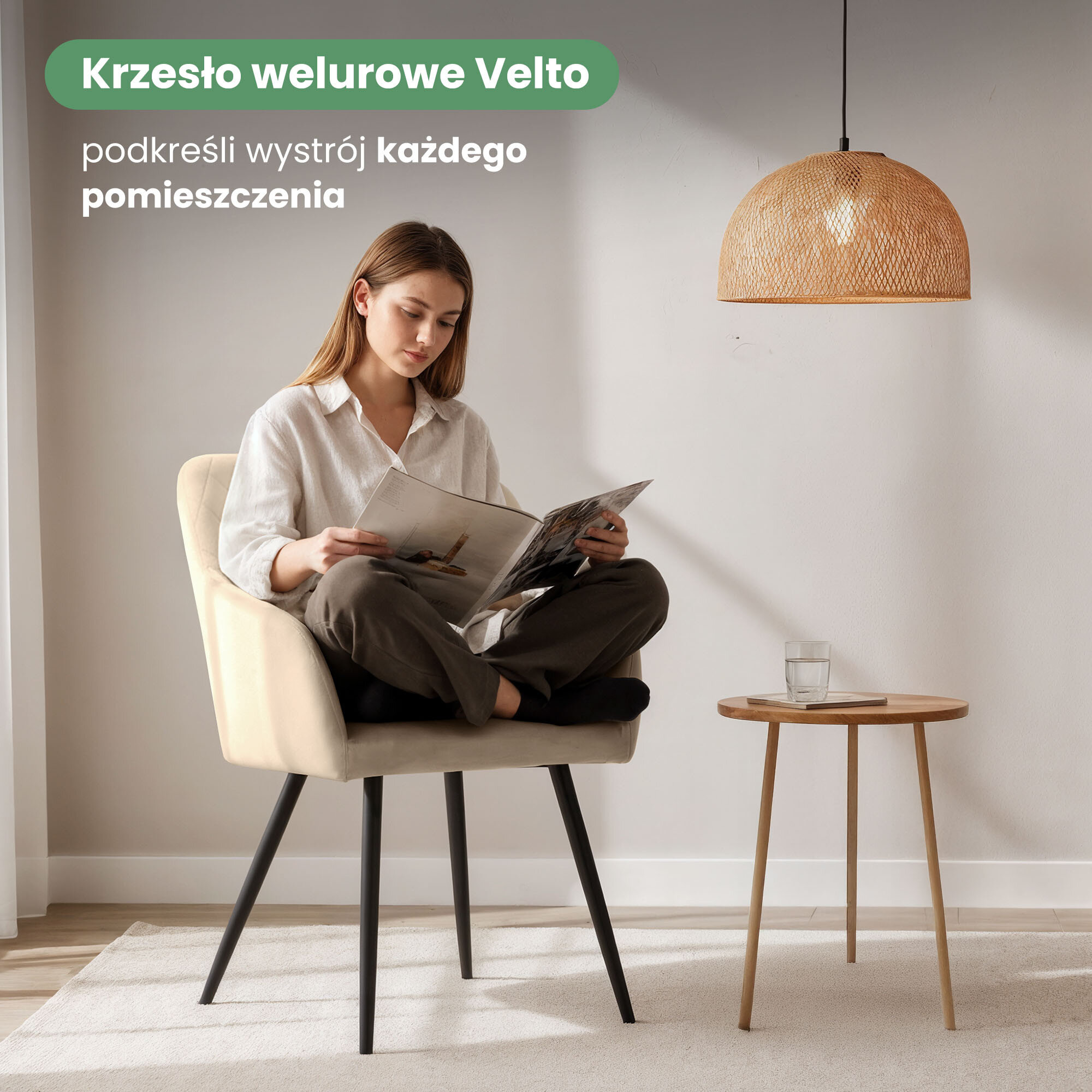Osoba siedzi na beżowym, welurowym krześle z czarnymi nogami, trzymając magazyn. Obok znajduje się mały stolik z szklanką wody, a nad nim wisi pleciona lampa sufitowa. Tekst na obrazie: \'Krzesło welurowe Velto podkreśli wystrój każdego pomieszczenia\'.