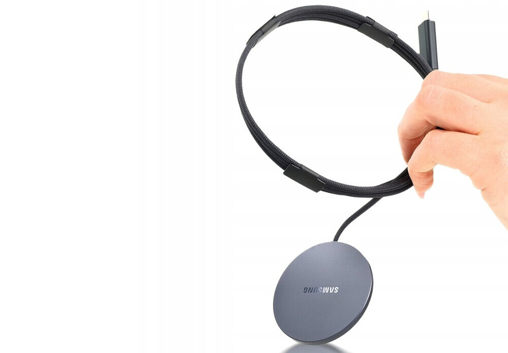 Osoba trzyma czarną ładowarkę indukcyjną z okrągłą podstawą, na której widnieje logo \'SAMSUNG\'.