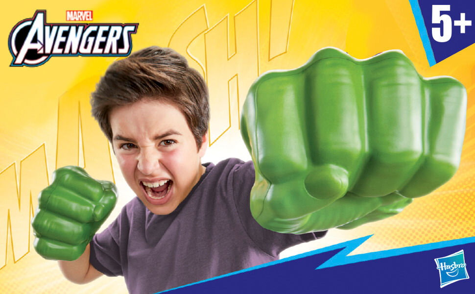 Rękawice HASBRO Marvel Avengers Gamma Smash Pięści Hulka F93325L0 Uśmiechnięty chłopiec w niebieskiej koszulce prezentuje duże, zielone rękawice Hulka od Hasbro. Rękawice mają realistyczną teksturę mięśni, wyrzeźbione kostki i paznokcie, imitując potężne pięści superbohatera Marvela.