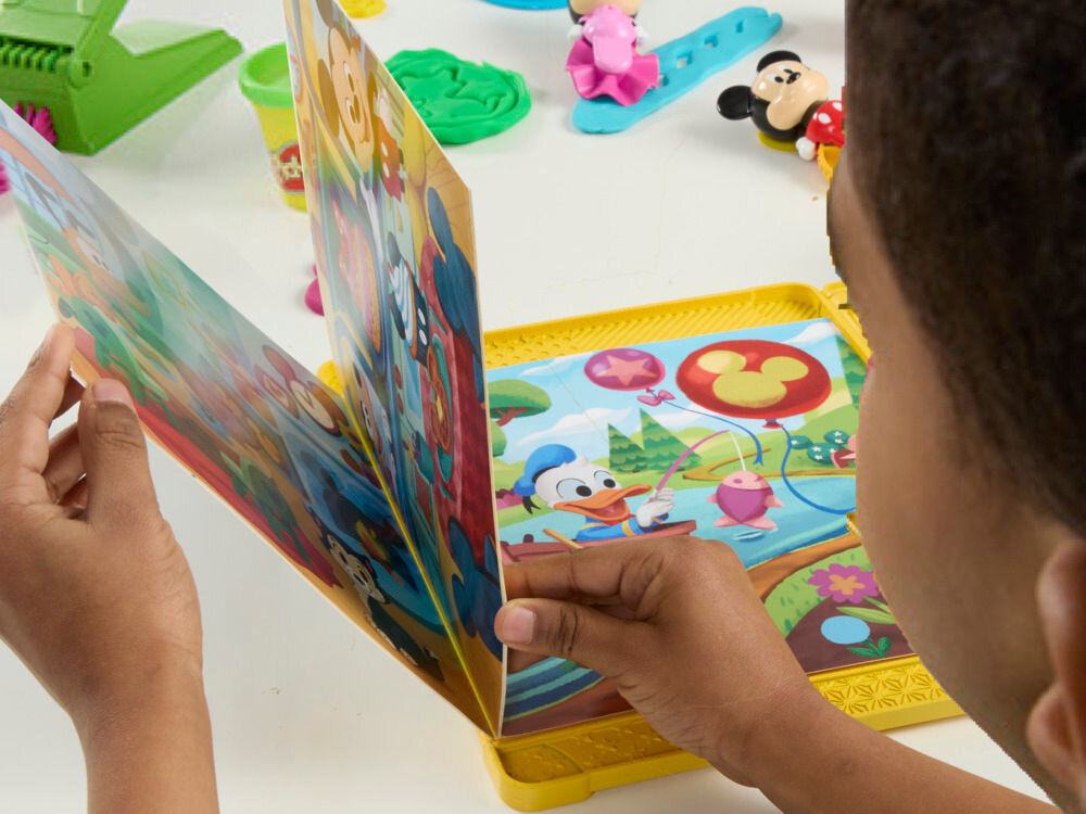 Ciastolina PLAY-DOH Disney Myszka Miki Ciastolinowe Opowieści G23245L0 Dziecko przewraca strony interaktywnej książeczki z zestawu Play-Doh Mickey Mouse Clubhouse, na której widać postać Kaczora Donalda w scenerii Disneya.