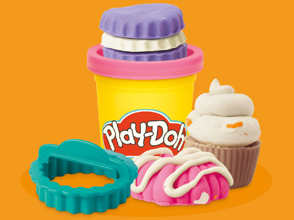 Ciastolina PLAY-DOH Małe przysmaki z cukierni G16155X0 Zbiór kolorowych kształtów uformowanych z ciastoliny Play-Doh, przedstawiających uśmiechnięte twarze Myszki Miki, Minnie, Daisy i psa Pluto obok żółtej kostki z tłoczonymi wzorami.