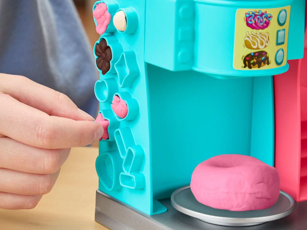 Ciastolina PLAY-DOH Pączkarnia G23085L0 Dziecięca dłoń wyjmująca małą gwiazdkę z różowej ciastoliny z foremek umieszczonych na bocznej ścianie maszynki Play-Doh.
