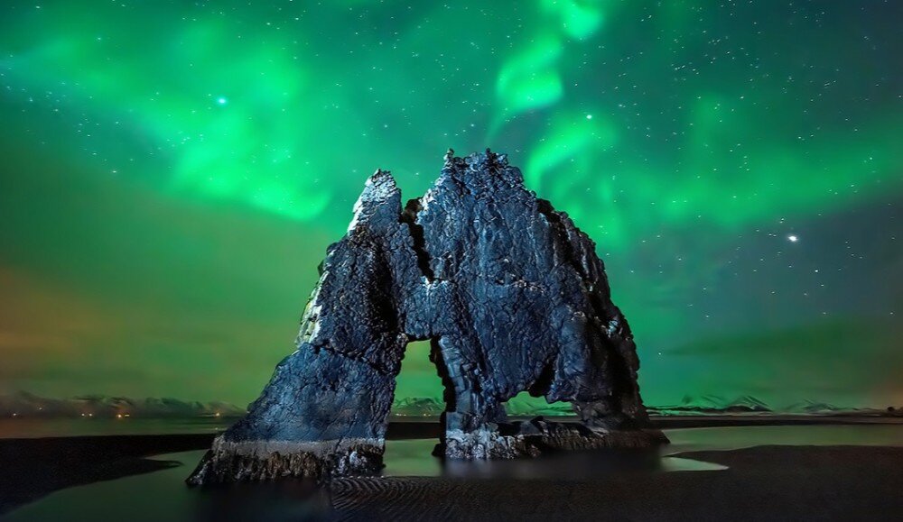 Monitor ACER Predator XB253QF Widok skały na tle zorzy polarnej, niebo rozświetlone zielonymi smugami zorzy, odbijającymi się delikatnie na tafli wody w dolnej części obrazu, kolory, sRGB