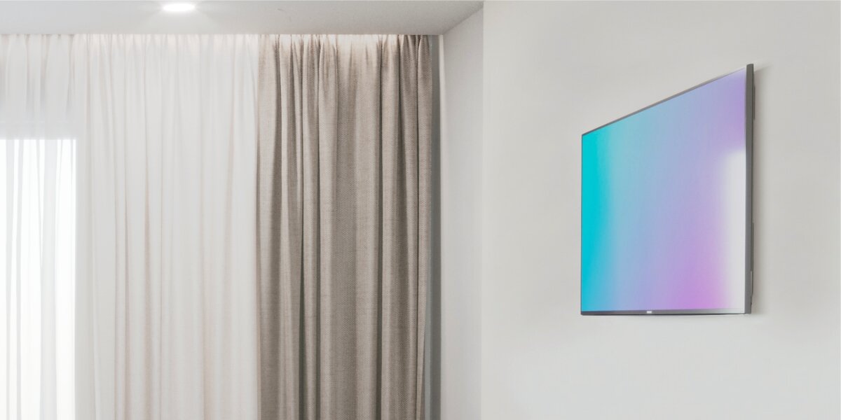 Telewizor zawieszony płasko na ścianie w minimalistycznym, domowym wnętrzu z zasłonami, prezentujący estetykę montażu uchwytu Hama FIX.
