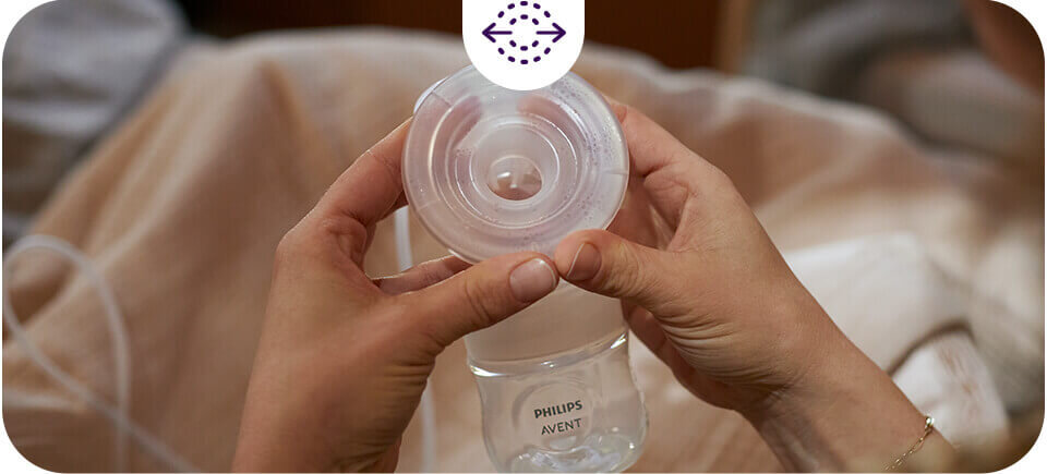 Osoba trzyma przezroczysty element laktatora marki Philips Avent. Na butelce widoczny jest napis \'PHILIPS AVENT\'.