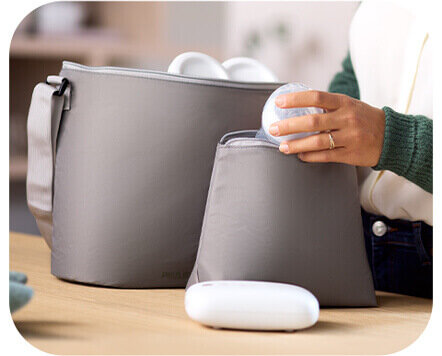 Osoba wkłada element laktatora do szarej torby na stole. Obok znajduje się druga, większa torba oraz biały element urządzenia.